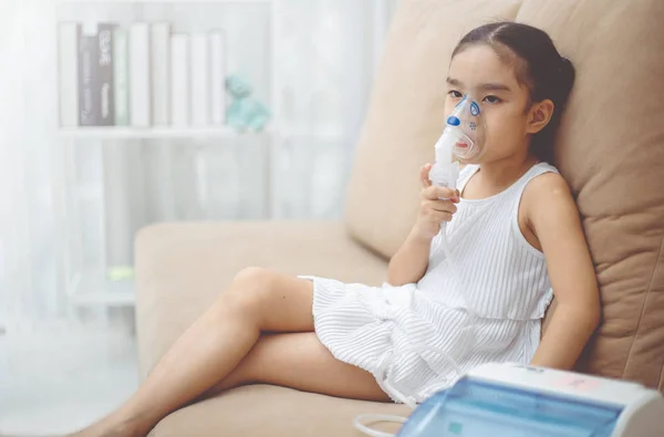 Cute Asian child  patient inhalation therapy by the mask of inhaler with soft stream smoke from bronchodilator.