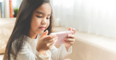 Bir smartphone kullanarak ve evde kanepede otururken gülümseyen şirin çocuk