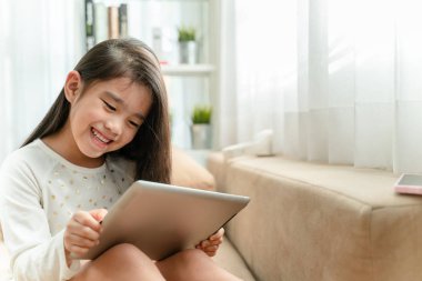 Tablet kullanma ve evde kanepede otururken gülümseyen şirin çocuk