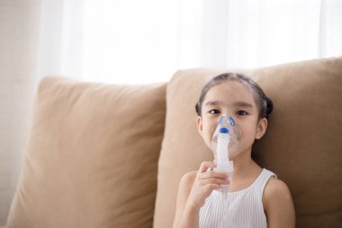 Cute Asian child patient inhalation therapy by the mask of inhaler with soft stream smoke from bronchodilator. clipart