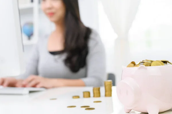 Bonito banco porquinho com moeda de ouro e borrão Mulher trabalhando em comput — Fotografia de Stock