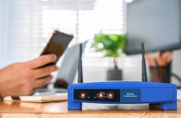 Nahaufnahme eines drahtlosen Routers und eines Mannes mit Smartphone auf livin — Stockfoto