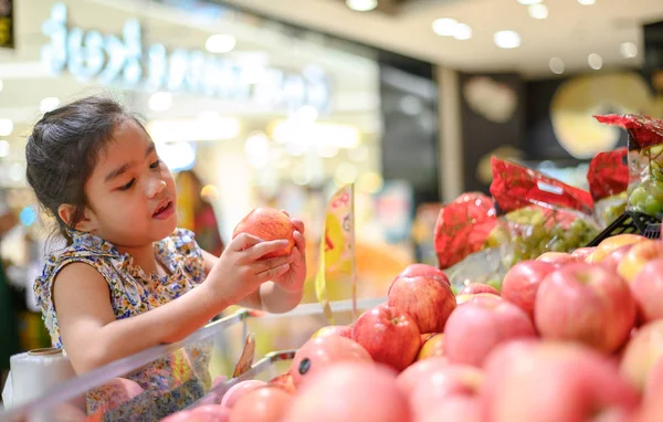 Asiático Niña elegir un manzana en un alimento tienda o un supermar — Foto de Stock
