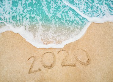 Mutlu Yıllar 2020 gün doğumu konseptinde deniz kıyısında kum yazılı.