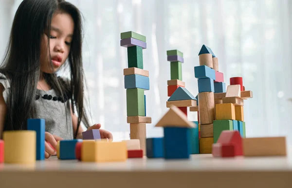 Happy little  girl playing game  building constructor tower from multicolored wooden blocks. learning and development background concept.