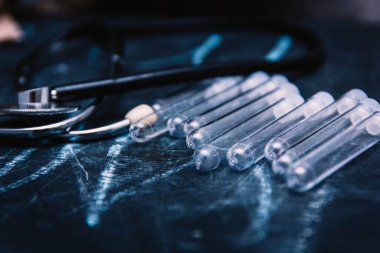 Tıbbi teşhis ve terapi konsepti, steteskop ve karanlık arka planda test tüpleri.