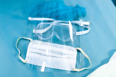 Mavi arka planda doktor, yüz kalkanı, gözlük ve maske için tıbbi koruyucu ekipman.