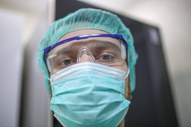 Gözlüklü ve koruyucu maskeli bir cerrah ameliyathanede çalışıyor.