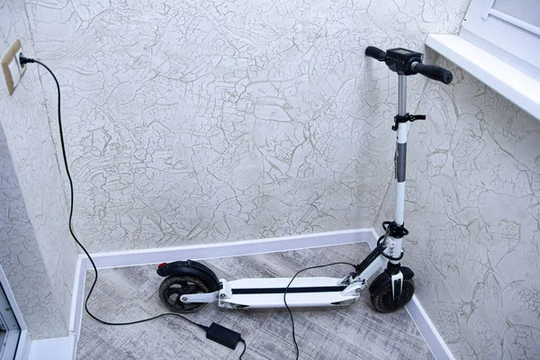 Yeni modern elektrikli scooter duvarın yanında şarj oluyor, yakın görüş 