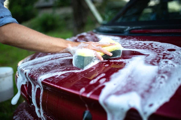 washing a red car with hands, a hook with foam on the back of a car.