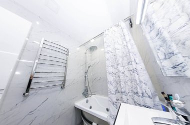 Modern bir banyo, ısıtılmış havlu rayı, lavabo ve seramik fayanslar - mermer taklidi.