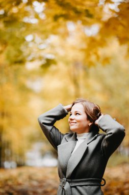 Gri montlu genç bir kadın sonbahar ormanında yürüyor. 