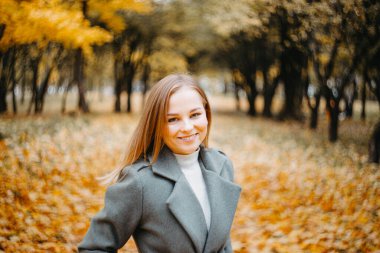 Gri montlu genç bir kadın sonbahar ormanında yürüyor. 