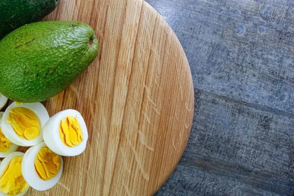 Cut boiled eggs with avocado on a wooden board in kitchen