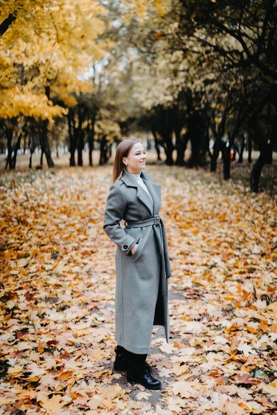 穿着灰色外套的年轻女子走在秋天的森林里 — 图库照片
