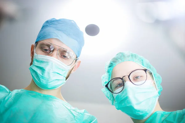 在医院手术室里有一名年轻的女助理实习生的专业外科医生 从较低的角度开枪 外科手术 — 图库照片