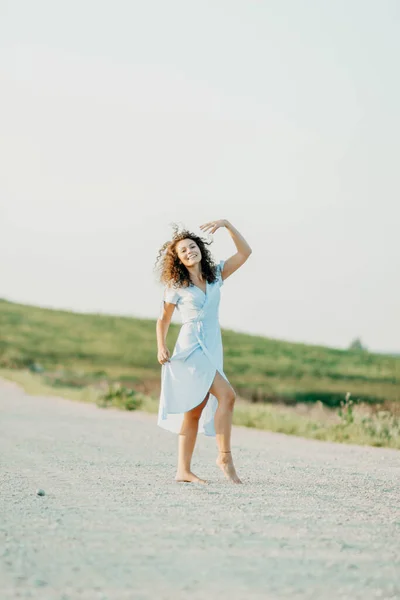 Кучерява Молода Жінка Танцює Романтично Блакитній Сукні Піщаній Дорозі Заході — стокове фото