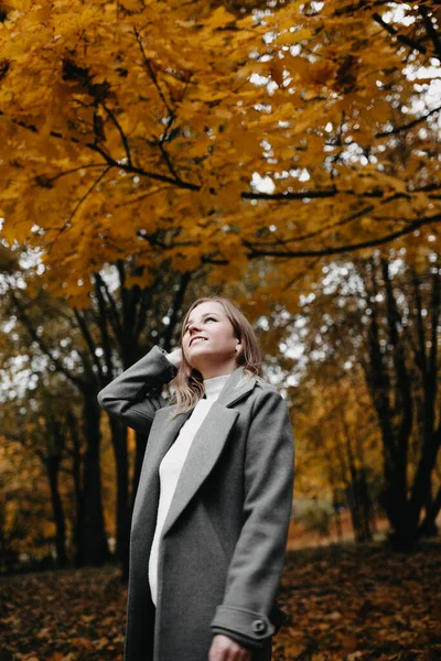 stock image Young woman in a gray coat walking in autumn forest 