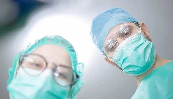 在医院手术室里有一名年轻的女助理实习生的专业外科医生 从较低的角度开枪 外科手术 — 图库照片