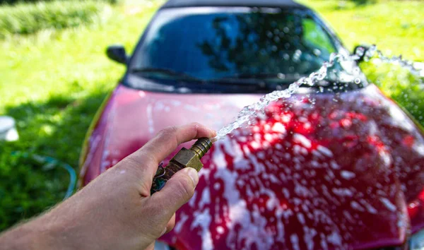 manual washing of a red car in the yard with a water hose.
