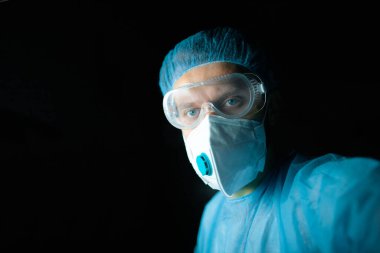 Üniformalı, gözlüklü ve sağlık maskeli bir erkek doktor ofiste çalışıyor. Profesyonel görünüm.