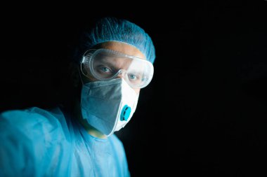 Üniformalı, gözlüklü ve sağlık maskeli bir erkek doktor ofiste çalışıyor. Profesyonel görünüm.