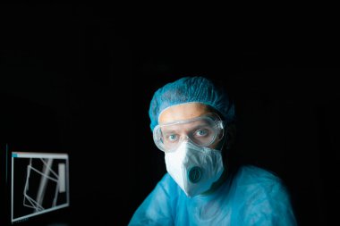 Karanlık bir laboratuvarda, monitörde kemik resmi olan ortopedik bir doktor..