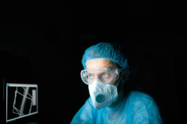 Karanlık bir laboratuvarda, monitörde kemik resmi olan ortopedik bir doktor..