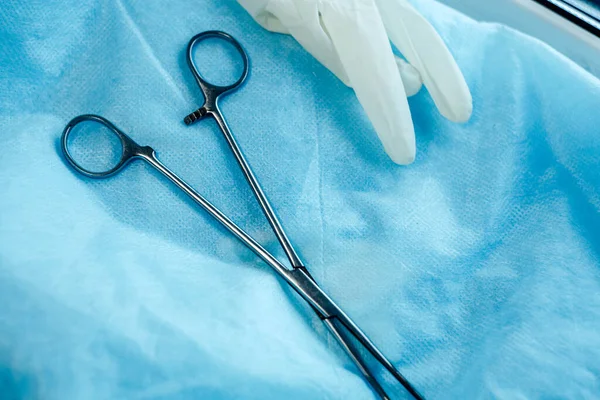 surgical instruments scissors and tweezers with gloves on a blue background.