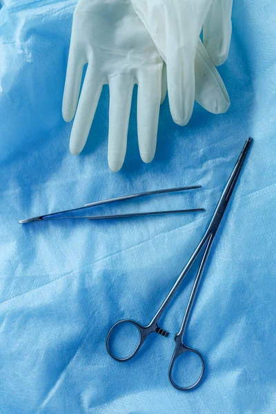 surgical instruments scissors and tweezers with gloves on a blue background.