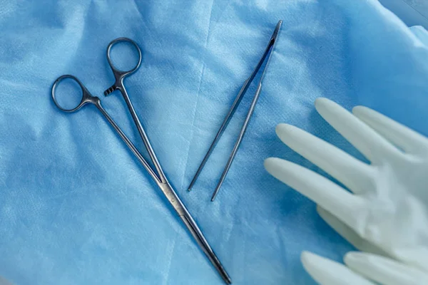 surgical instruments scissors and tweezers with gloves on a blue background.