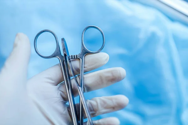 surgical scissors in the hand of the surgeon on a blue background. Surgery concept