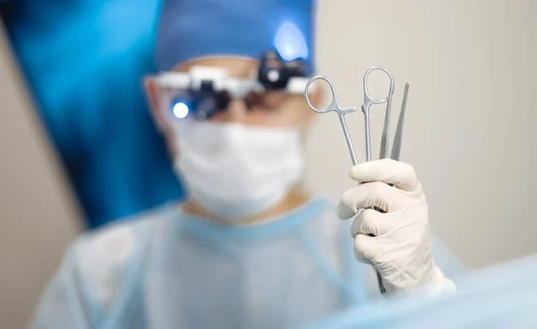 male surgeon holds in hand surgical instruments tweezers and scissors clamps.