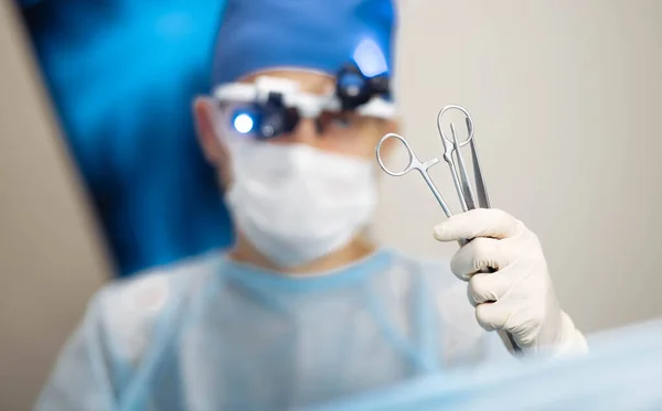 male surgeon holds in hand surgical instruments tweezers and scissors clamps.