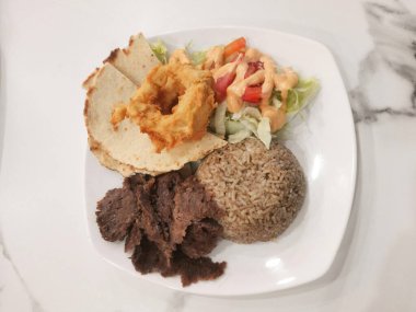 Tüylü pirinç, taze salata ve kızarmış soğan halkalarının eşlik ettiği leziz bir donör kebabı sunan güzel bir tabak..