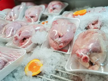 Yakın plan çekimlerde çeşitli soğutulmuş, paketlenmiş tavuklar süpermarket buzdolabının içinde buzdan bir yatakta düzgünce dizilmiş. Tavukların arasında portakal dilimleri var.,