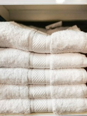 Eşsiz bir desenli bandı olan el değmemiş beyaz havlular. Rafta düzgünce düzenlenmiş. Yumuşaklık, temizlik ve evcil alanlarda rafine rahatlık için ideal..