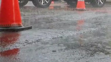 Yağmurlu bir günün atmosferini bu yansımayla yaşayın, su damlacıkları asfaltta su birikintileri yaratırken, ve trafik konileri park halindeki arabaların arasında dururken