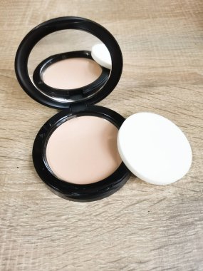 Yakın çekim, kırsal ahşap bir yüzeye yerleştirilmiş bir yüz pudrası ve aplikatörü yakalar. Tozun tarafsız tonları kişisel ilgiyi vurgular.