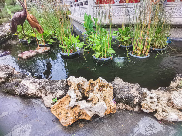 A beautiful outdoor landscape features a tranquil pond with lush plants and elegant sculptures. The tranquil landscape creates a sense of peace and harmony. Textured rocks enhance the natural beauty.