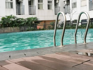 Bir apartman kompleksinde turkuaz su ve modern konfor içeren huzurlu bir yüzme havuzu görüntüsü. Dinginlik ve rahatlama için mükemmel bir ortam..