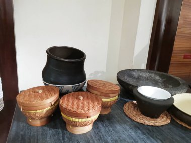 Bir yüzeyde seramik çömlek, dokuma sepetleri ve taş havan topları koleksiyonu sergilenirken, iç dekorasyon ve sanatsal düzenlemeler için rustik ve çağdaş tasarım unsurlarının bir karışımı sergilenmektedir..