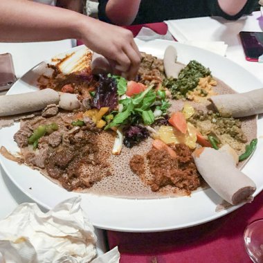 Hands eating from Ethiopian meal with injera bread and various stews clipart