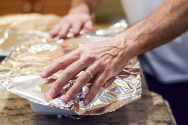 Güveç çanağı fırında yedeklemek için alüminyum folyo ile kaplayan eller