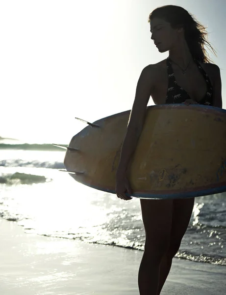 海のそばの砂浜に立ってサーフボードを持っている女性 — ストック写真