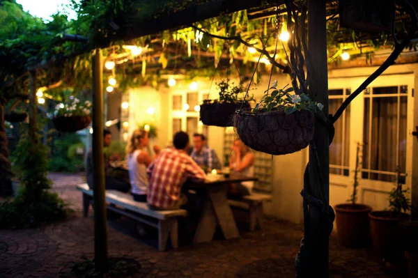 Group People Sitting Outdoors Table Hanging Baskets Foreground Evening — Stock Photo, Image