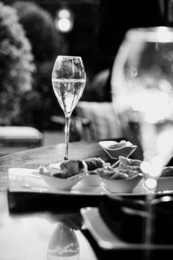 Şampanya bardağı ve gurme aperatiflerinin açık hava etkinliklerindeki siyah beyaz görüntüsü. Ayarlar sofistike bir atmosfer olduğunu gösteriyor. Kutlamalar için mükemmel.