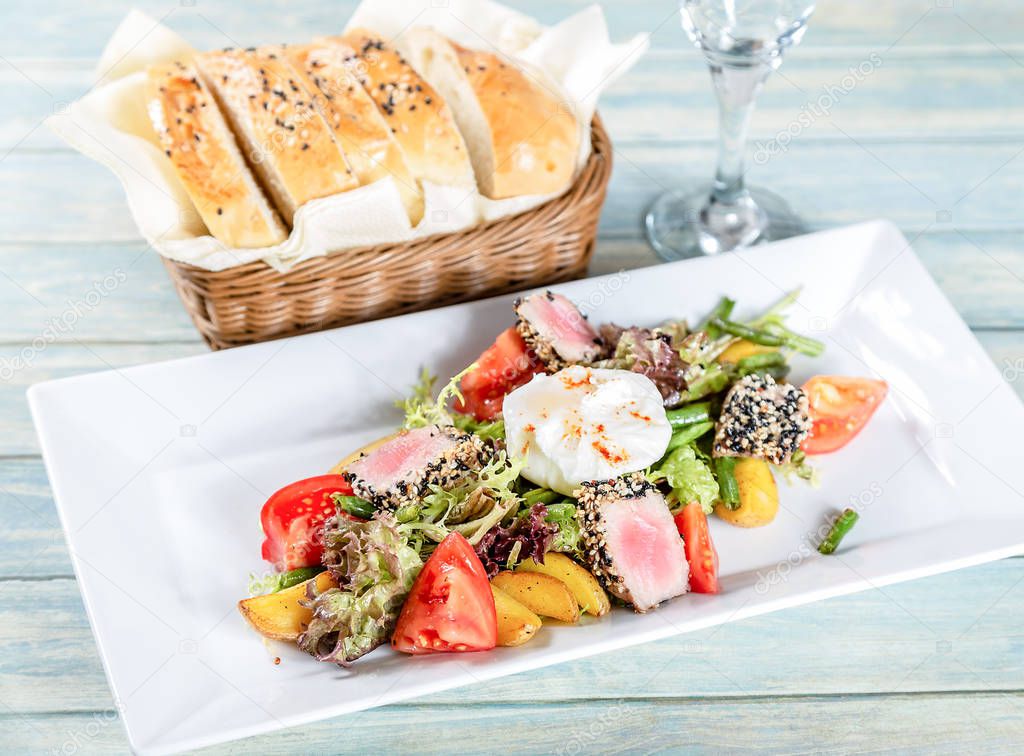 Plate of nicoise salad with roasted tuna and poached egg on wooden table