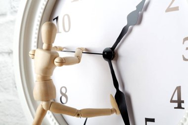 Ahşap insan figürü saatin oku durdurmaya çalışırken. Yaşlanma, koruma kavramı