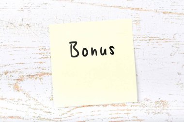 El yazısı metnini bonus ile ahşap masa üzerinde sarı yapışkan not